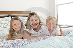 Young blond Caucasian woman lying on bed together with her little sweet 3 and 7 years old son and daughter smiling playful and hap