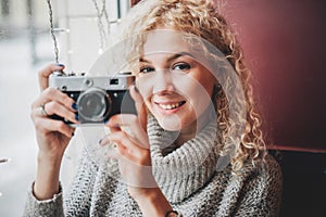 Young blond curly female with old film camera in cafe