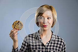 Young blond cute and friendly caucasian woman in casual clothes holding big delicious chocolate cookie