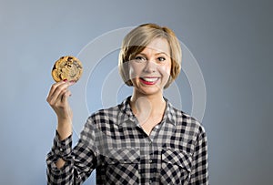 Young blond cute and friendly caucasian woman in casual clothes holding big delicious chocolate cookie