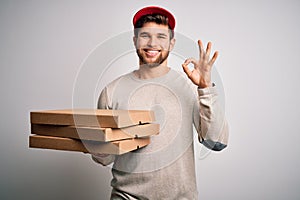 Young blond delivery man with beard and blue eyes holding cardboards of pizza doing ok sign with fingers, excellent symbol