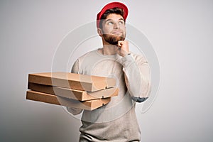 Young blond delivery man with beard and blue eyes holding cardboards of pizza serious face thinking about question, very confused