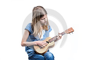 Young, blond girl in blue T-shirt is playing music on ukulele instrument