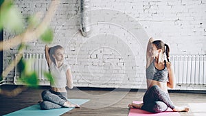 Young blond girl is enjoying individual yoga practice with friendly female instructor in light studio. Women are doing