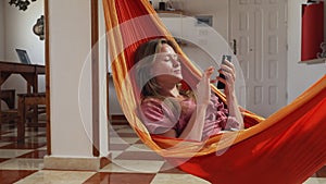 Young blond girl lying in hammock at home and using her smartphone