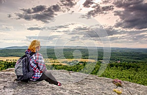 A young blond girl sit on peak and enjoy sun. Woman hiker