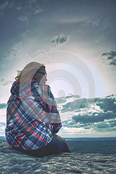 A young blond girl sit on peak and enjoy sun. Woman hiker