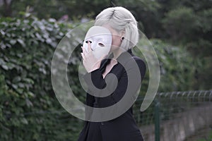 Young blond girl taking off a mask. Pretending to be someone else concept. outdoors. photo