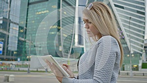 A young blond girl uses a tablet on a background of skyscrapers downtown.