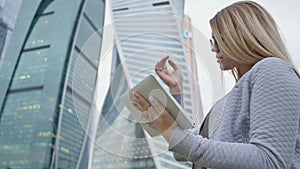 A young blond girl uses a tablet on a background of skyscrapers downtown.