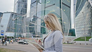 A young blond girl uses a tablet on a background of skyscrapers downtown.