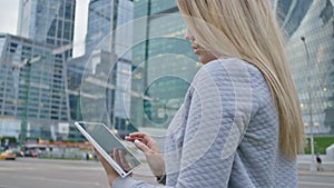 A young blond girl uses a tablet on a background of skyscrapers downtown.