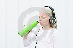 Young blond girl on white background drink fresh spring water from green reusable bottle.