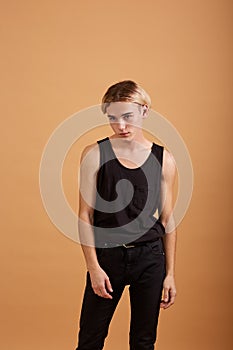 Young blond guy dressed in a black t-shirt and pants posing in the studio on the beige background