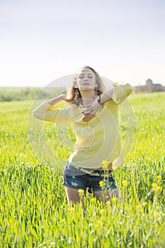 Young blond hair woman poses in a summer green wheat field