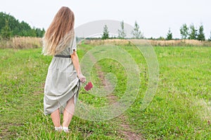 Young blond long haired woman with red abloom dahlia flower in yand stand on road with green grass.