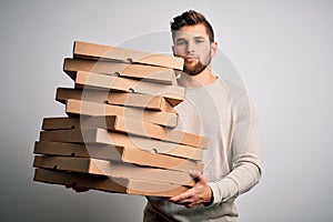 Young blond man with beard and blue eyes holding cardboards of pizza over white background with a confident expression on smart