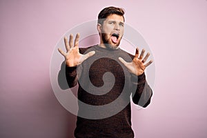 Young blond man with beard and blue eyes wearing casual sweater over pink background afraid and terrified with fear expression