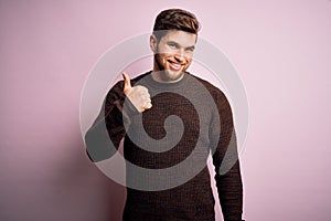 Young blond man with beard and blue eyes wearing casual sweater over pink background doing happy thumbs up gesture with hand