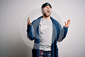 Young blond man with beard and blue eyes wearing sleep mask and pajama crazy and mad shouting and yelling with aggressive