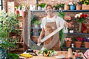 Young blond man florist smiling confident holding gift lace at flower shop