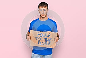 Young blond man holding power to the people banner thinking attitude and sober expression looking self confident