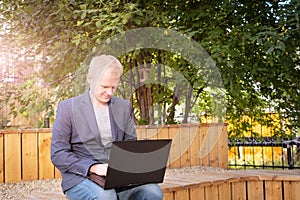 Young blond man in a jacket with a laptop.
