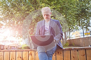 Young blond man in a jacket with a laptop.