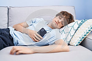 Young blond man listening to music sleeping on sofa at home