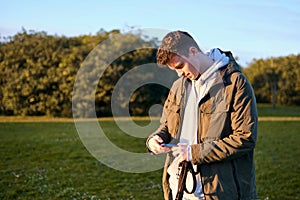 Young blond man looking with interest and strangeness at the screen of his mobile phone in a park