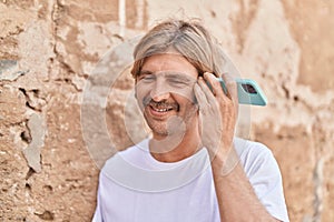 Young blond man miling confident listening audio message by the smartphone at street