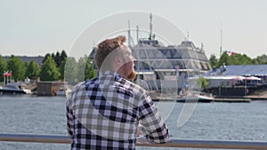 Young blond man walks by the water. Pensive guy is enjoying nature. a man in a checkered shirt walks