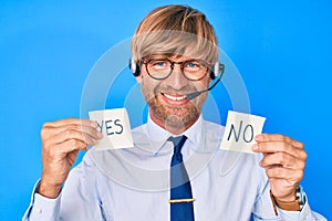 Young blond man wearing operator headset holding yes and no reminder smiling with a happy and cool smile on face