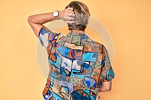 Young blond man wearing summer shirt backwards thinking about doubt with hand on head