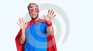 Young blond man wearing super hero custome afraid and terrified with fear expression stop gesture with hands, shouting in shock