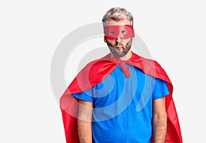 Young blond man wearing super hero custome making fish face with lips, crazy and comical gesture