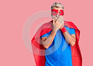 Young blond man wearing super hero custome shocked covering mouth with hands for mistake