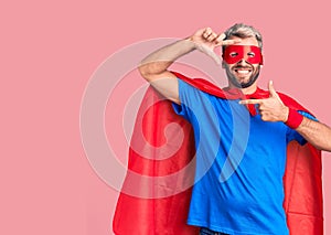 Young blond man wearing super hero custome smiling making frame with hands and fingers with happy face