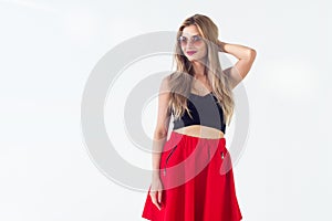 Young blond model presenting new fashionable summer look, wearing circle sunglasses, red skirt and black sleeveless top