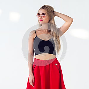 Young blond model presenting new fashionable summer look, wearing circle sunglasses, red skirt and black sleeveless top
