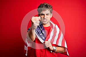 Young blond patriotic man with curly hair wearing USA flag celebrating independence day annoyed and frustrated shouting with