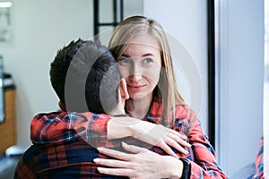 Young blond pretty woman, hugging brunette man,with his back to camera. Romantic couple, wearing red casual checkered shirts,