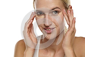 Young blond smiling woman applying concealer under her eyes