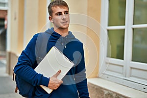 Young blond student smiling happy holding notebook at the university