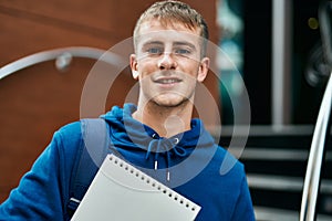 Young blond student smiling happy holding notebook at the university