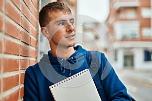 Young blond student smiling happy holding notebook at the university