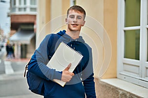 Young blond student smiling happy holding notebook at the university