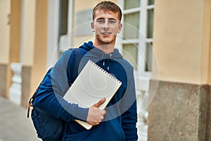 Young blond student smiling happy holding notebook at the university