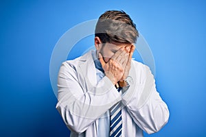 Young blond therapist man with beard and blue eyes wearing coat and tie over background with sad expression covering face with