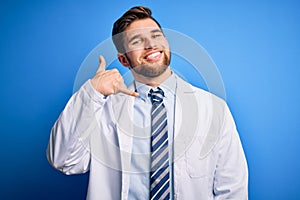 Young blond therapist man with beard and blue eyes wearing coat and tie over background smiling doing phone gesture with hand and